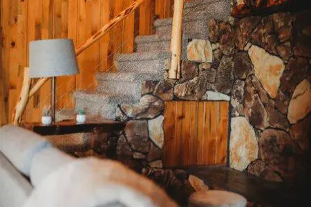 Cozy interior with stone accent wall, carpeted stairs, and log railing in a Fairbanks Alaska treehouse rental