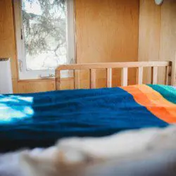 Sunlit bed with colorful blanket in a wood-paneled room of a Fairbanks Alaska treehouse rental