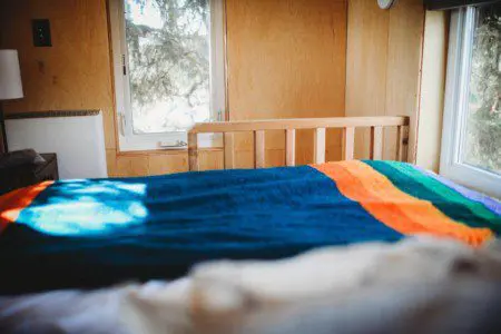 Sunlit bed with colorful blanket in a wood-paneled room of a Fairbanks Alaska treehouse rental