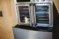 Close-up of a mini fridge and stainless steel countertop oven in a wood-paneled Fairbanks Alaska treehouse