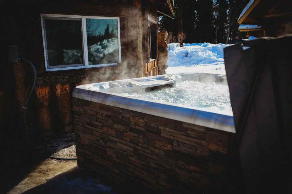 Steaming outdoor hot tub beside rustic wood cabin in snowy Fairbanks Alaska setting