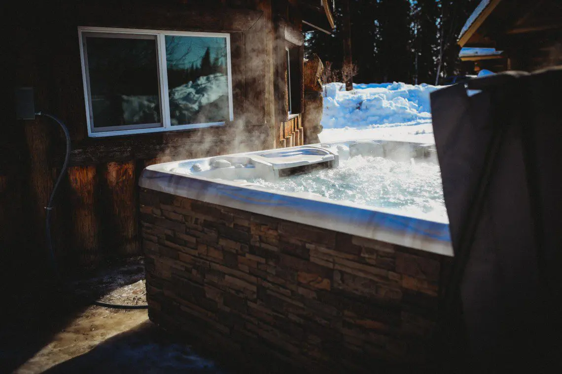 Steaming outdoor hot tub beside rustic wood cabin in snowy Fairbanks Alaska setting