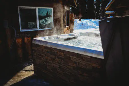 Steaming outdoor hot tub beside rustic wood cabin in snowy Fairbanks Alaska setting