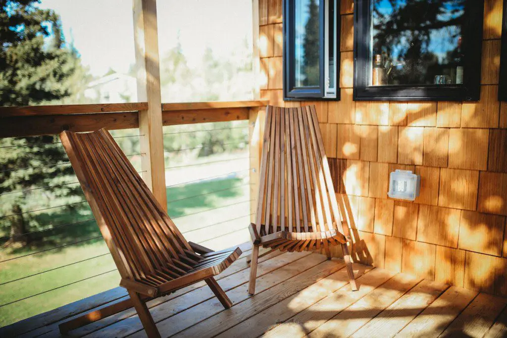 Wooden chairs on a sunny outdoor deck of a Fairbanks Alaska treehouse rental with natural views