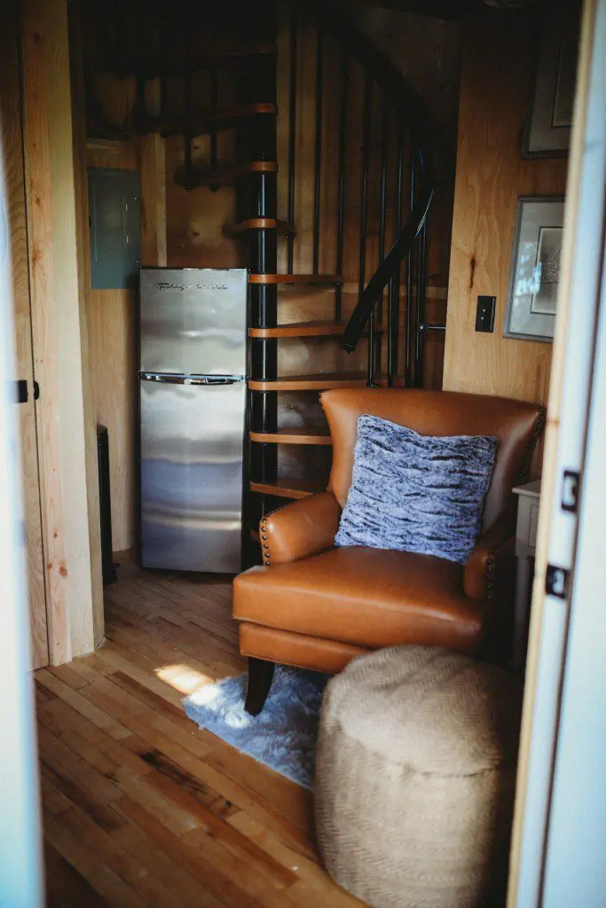 Cozy interior of Fairbanks Alaska treehouse with spiral staircase, leather chair, and loft netting