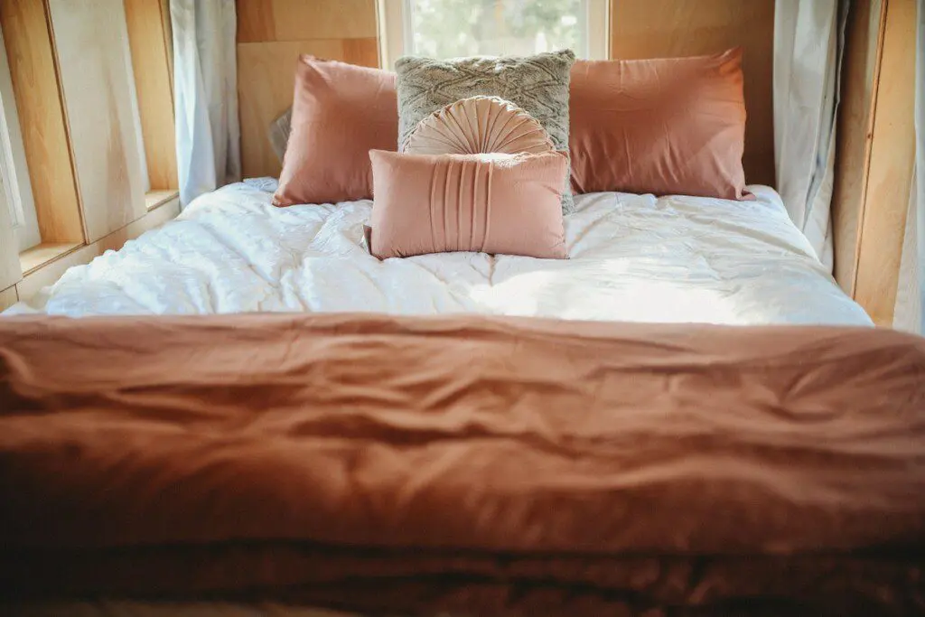 Inviting bed with soft pillows and warm-toned bedding in a wood-paneled Fairbanks Alaska treehouse rental