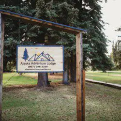 Wooden sign for Alaska Adventure Lodge with trees in the background, located in Fairbanks, Alaska