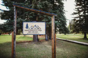 Wooden sign for Alaska Adventure Lodge with trees in the background, located in Fairbanks, Alaska