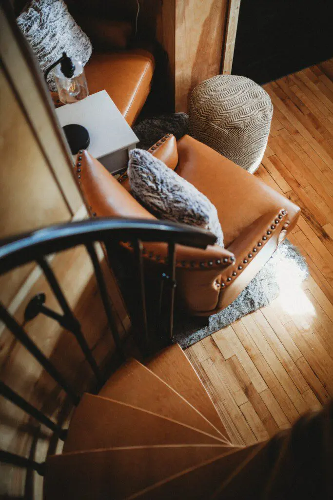Leather armchair with textured pillows next to spiral staircase in Alaska treehouse rental