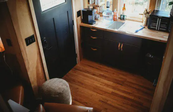 Compact kitchen area with dark cabinets, wooden floor, and window view in a Fairbanks Alaska treehouse rental