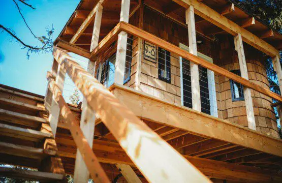 Wooden structure of a rustic treehouse with elevated balcony and stairs under clear blue sky in Fairbanks Alaska