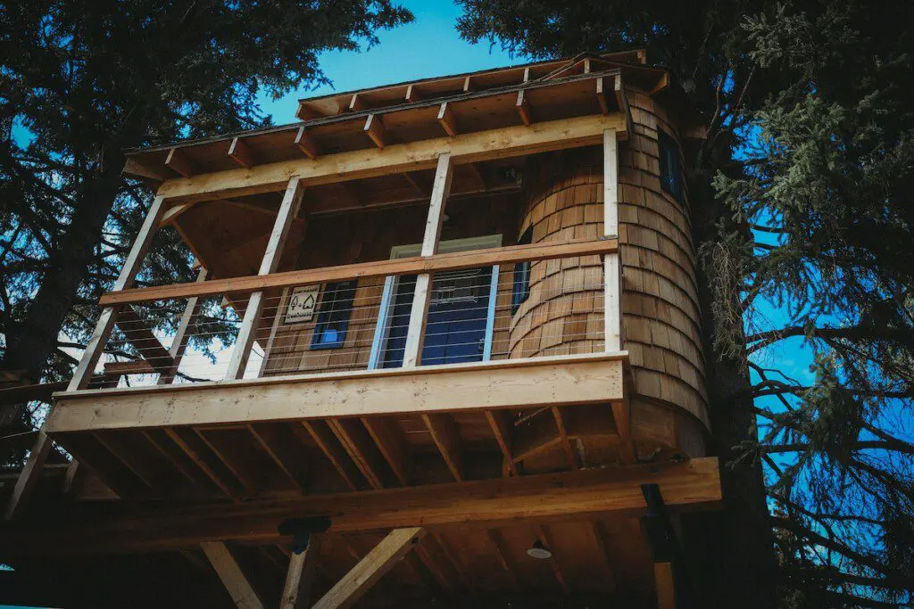 Elevated wooden treehouse cabin surrounded by pine trees in Fairbanks, Alaska.
