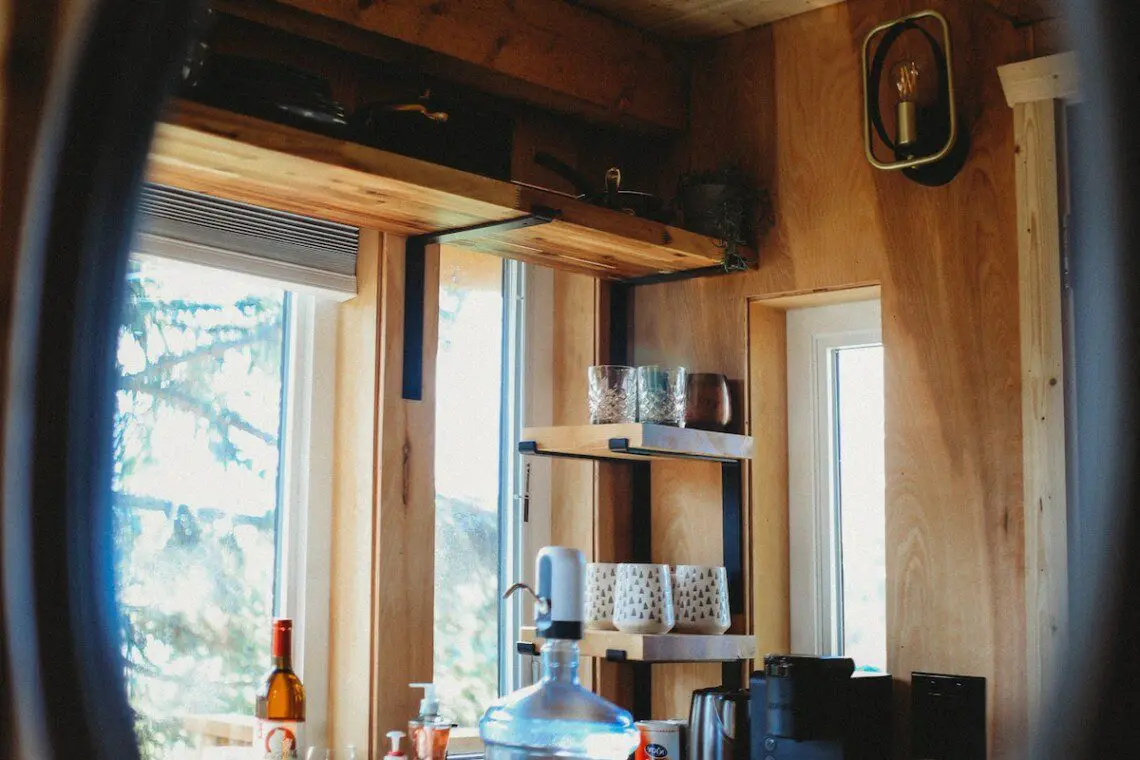 Rustic kitchenette with wooden shelves, water dispenser, mugs, and coffee essentials in a Fairbanks Alaska treehouse