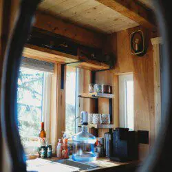 Rustic kitchenette with wooden shelves, water dispenser, mugs, and coffee essentials in a Fairbanks Alaska treehouse