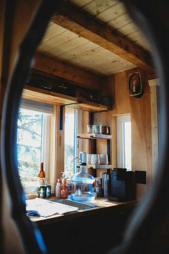 Rustic kitchenette with wooden shelves, water dispenser, mugs, and coffee essentials in a Fairbanks Alaska treehouse