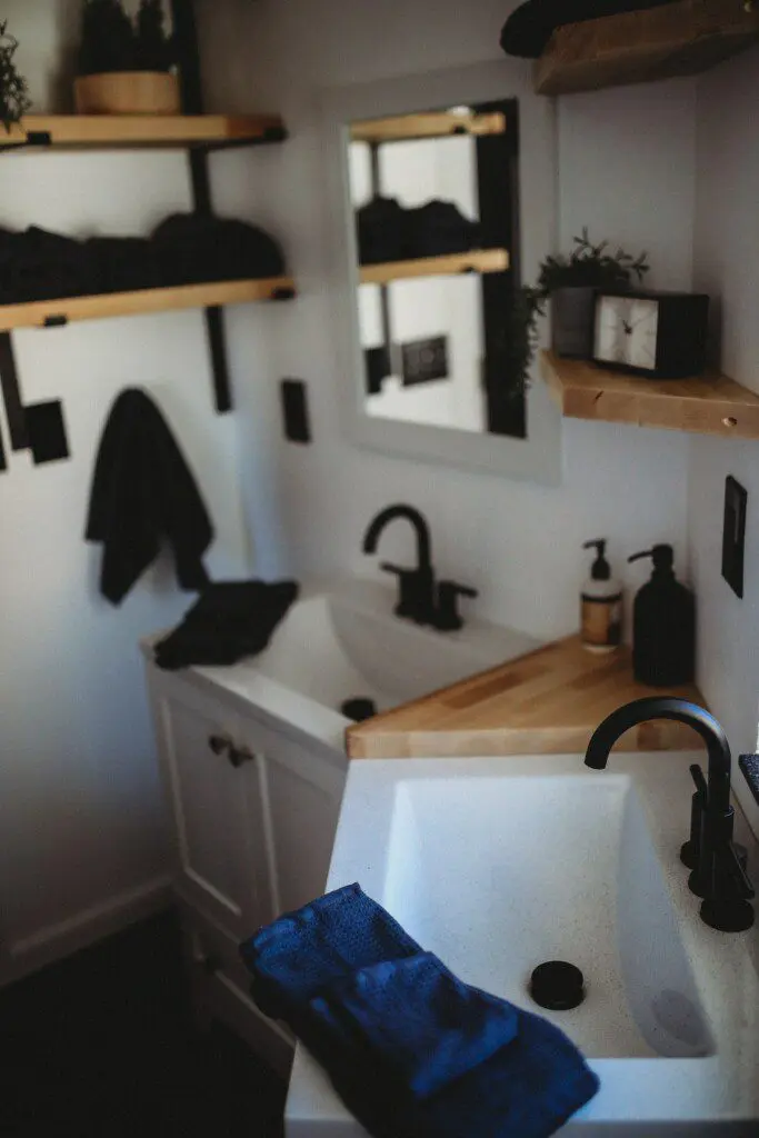 Modern double-sink bathroom with black fixtures and wood shelving in a Fairbanks Alaska treehouse rental.