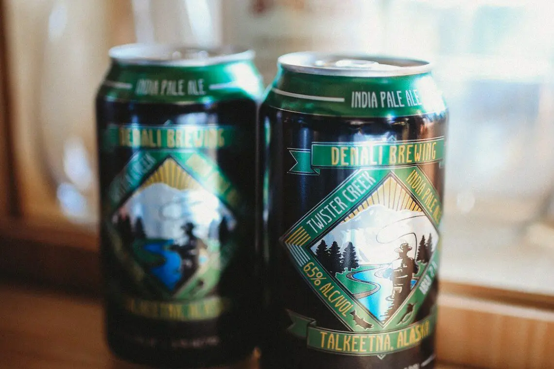 Two cans of local craft beer on a wooden counter inside a cozy Alaska adventure lodge near Fairbanks