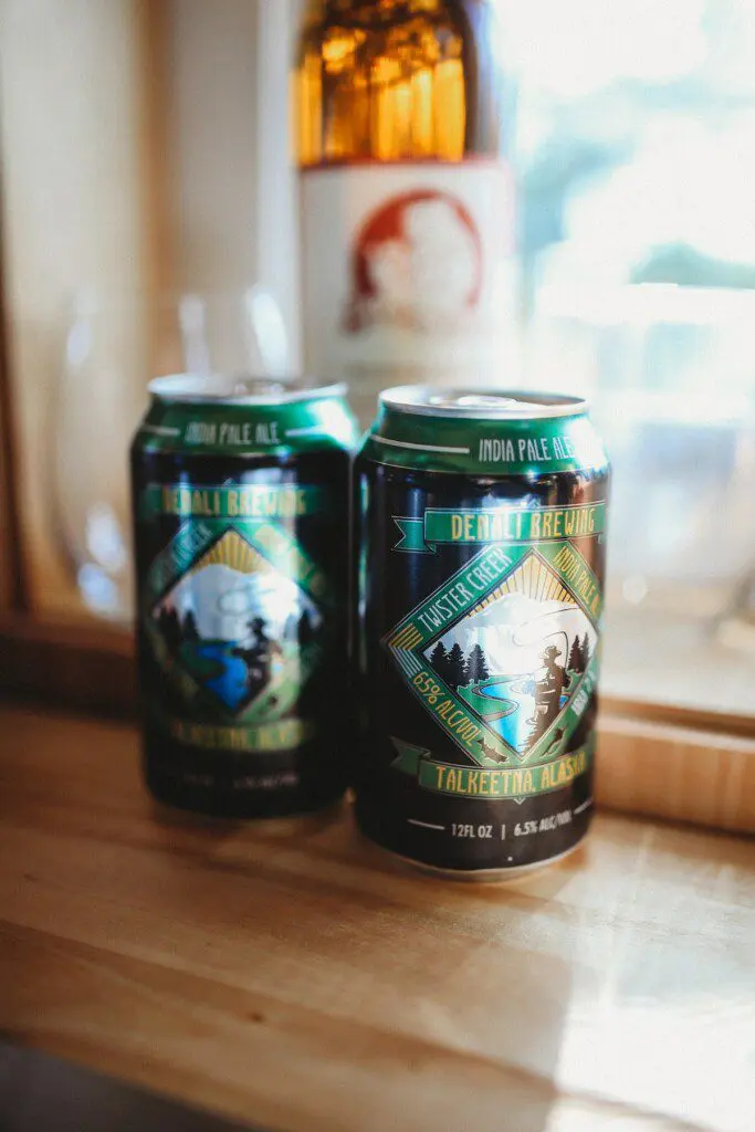 Two cans of local craft beer on a wooden counter inside a cozy Alaska adventure lodge near Fairbanks