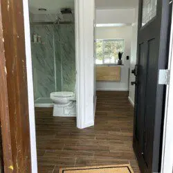 Open black door revealing a clean bathroom with glass shower and wood-look tile flooring in a Fairbanks rental