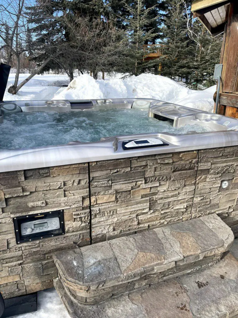 Bubbling outdoor hot tub with stone siding in a snowy Fairbanks Alaska forest setting