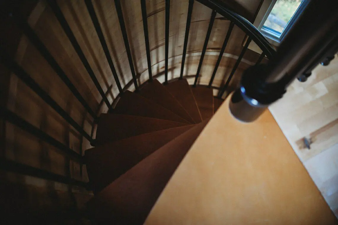 Top-down view of a wooden spiral staircase with black railing in a cozy Fairbanks Alaska treehouse rental