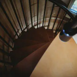 Top-down view of a wooden spiral staircase with black railing in a cozy Fairbanks Alaska treehouse rental