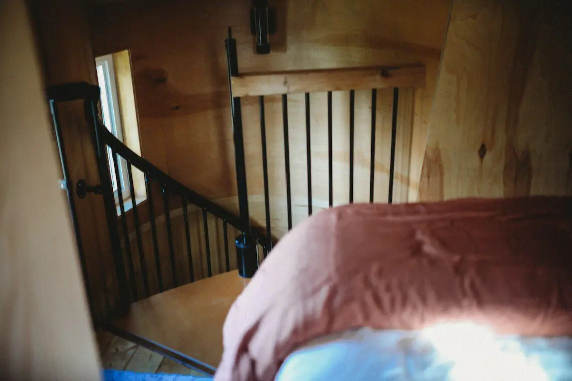 Cozy loft bedroom with wood walls and spiral staircase in a Fairbanks Alaska adventure lodge or treehouse rental