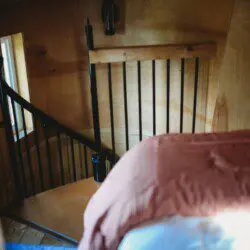 Cozy loft bedroom with wood walls and spiral staircase in a Fairbanks Alaska adventure lodge or treehouse rental