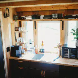 Wood and black kitchen with large windows, coffee setup, and natural light in a Fairbanks Alaska treehouse rental