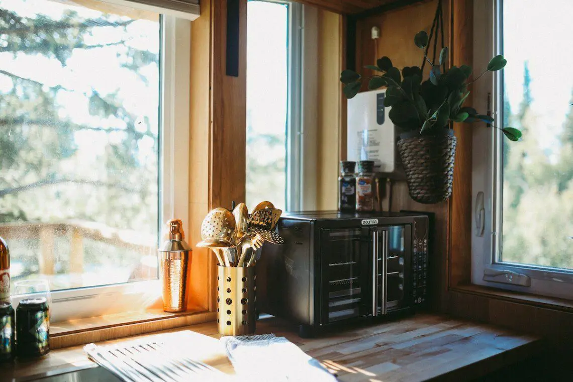 Rustic kitchenette with wooden shelves, water dispenser, mugs, and coffee essentials in a Fairbanks Alaska treehouse