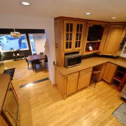 Spacious dining room with a large wooden table, modern chairs, and floor-to-ceiling windows showcasing a snowy forest at an Alaska lodge.