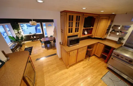 Spacious dining room with a large wooden table, modern chairs, and floor-to-ceiling windows showcasing a snowy forest at an Alaska lodge.