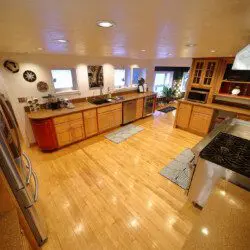 Spacious dining room with a large wooden table, modern chairs, and floor-to-ceiling windows showcasing a snowy forest at an Alaska lodge.