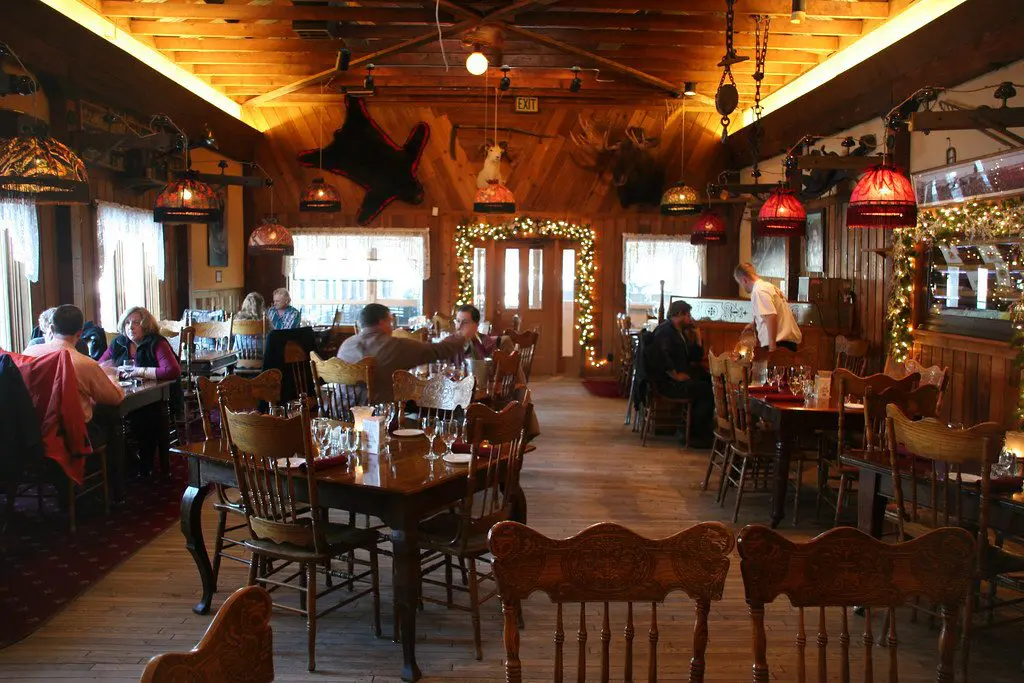 Rustic wood interior of an Alaskan lodge-style restaurant with guests dining under warm lighting