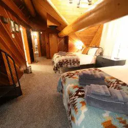 Rustic loft bedroom with two beds, patterned blankets, and log cabin walls in Fairbanks Alaska
