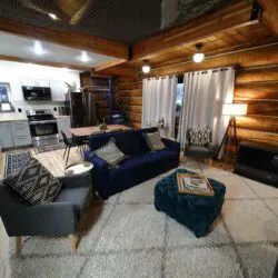 Modern open-concept living area with navy couch, kitchen, and spiral staircase in a Fairbanks Alaska treehouse rental
