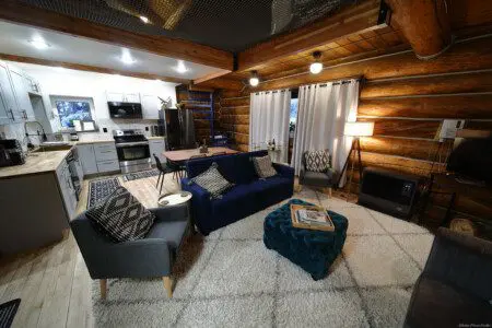 Modern open-concept living area with navy couch, kitchen, and spiral staircase in a Fairbanks Alaska treehouse rental