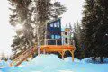Modern black and wood-paneled treehouse rental elevated on stilts in a snowy forest in Fairbanks, Alaska.