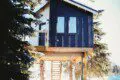Modern black and wood-paneled treehouse rental elevated on stilts in a snowy forest in Fairbanks, Alaska.