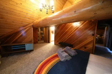 Cozy attic-style bedroom with wood-paneled walls, exposed beam, and folded towels in a Fairbanks lodge