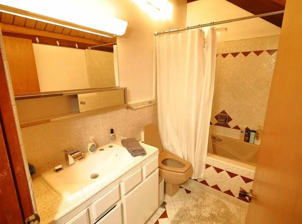 Rustic log cabin bathroom with white vanity, shower curtain, and wood-accented ceiling at Alaska Adventure Lodge in Fairbanks, Alaska