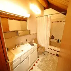 Rustic log cabin bathroom with white vanity, shower curtain, and wood-accented ceiling at Alaska Adventure Lodge in Fairbanks, Alaska
