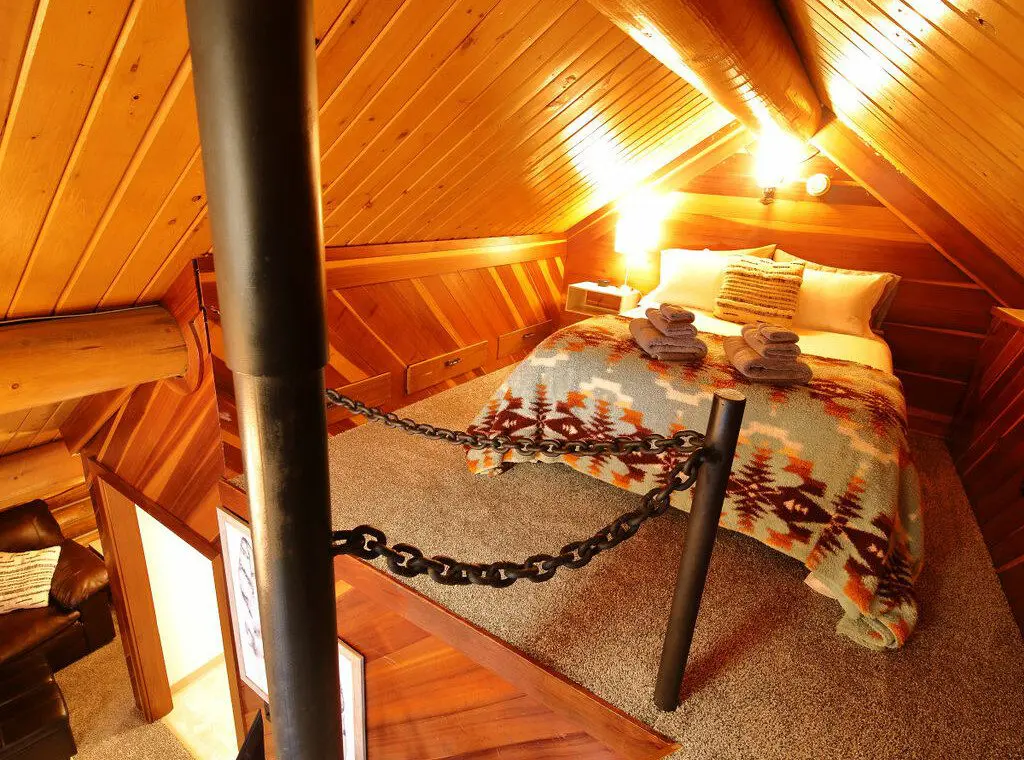 Rustic cabin bedroom with tribal blanket, soft lighting, and wooden walls in a Fairbanks, Alaska treehouse rental.