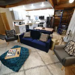Modern open-concept living area with navy couch, kitchen, and spiral staircase in a Fairbanks Alaska treehouse rental