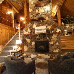 Cozy log cabin living room with stone fireplace, modern sofa, and wood carvings in Fairbanks Alaska