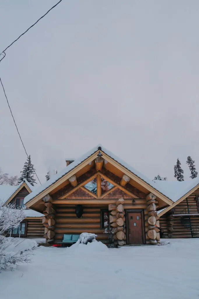 Snow-covered log cabin with wood carvings and peaked roof in Fairbanks, Alaska