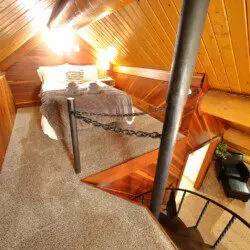 Rustic log cabin bedroom with cozy bedding and spiral staircase in Fairbanks Alaska