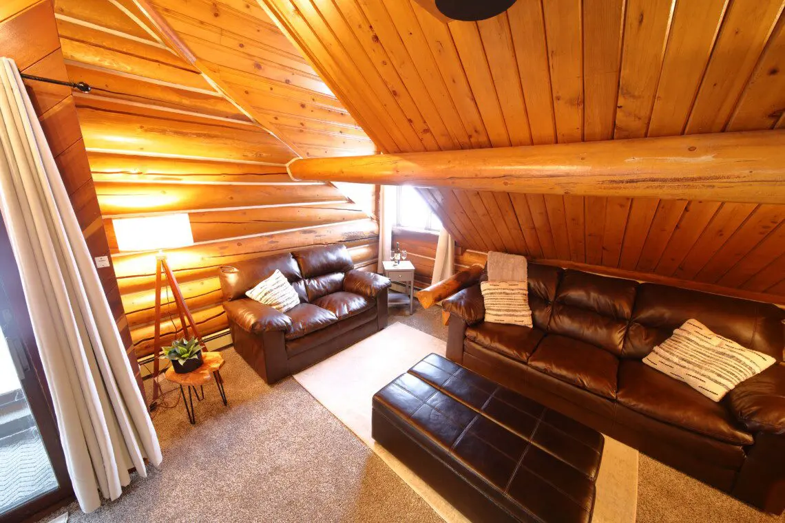 Cozy upstairs lounge with leather sofas, wood-paneled ceiling, and soft lighting at Alaska Adventure Lodge in Fairbanks, Alaska