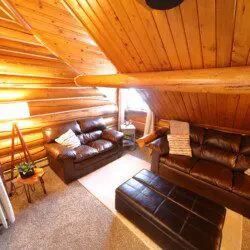 Cozy upstairs lounge with leather sofas, wood-paneled ceiling, and soft lighting at Alaska Adventure Lodge in Fairbanks, Alaska