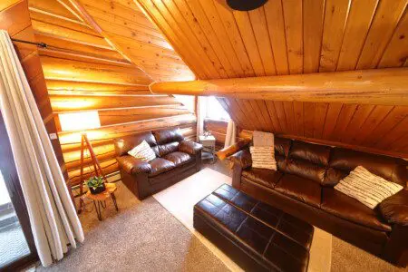 Cozy upstairs lounge with leather sofas, wood-paneled ceiling, and soft lighting at Alaska Adventure Lodge in Fairbanks, Alaska